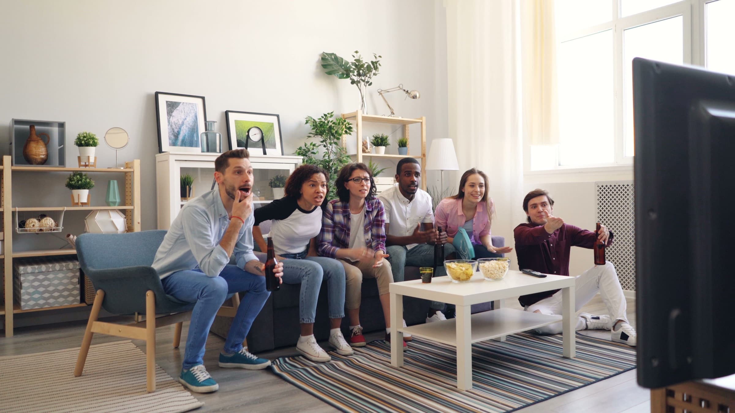 Un groupe d'amis réunis sur un canapé regarde la télévision dans un salon lumineux